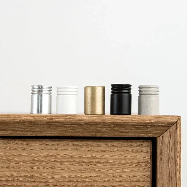 Knapper i metal i forskellige farver på toppen af et egetræsmøbel, ideelle til dansk design.